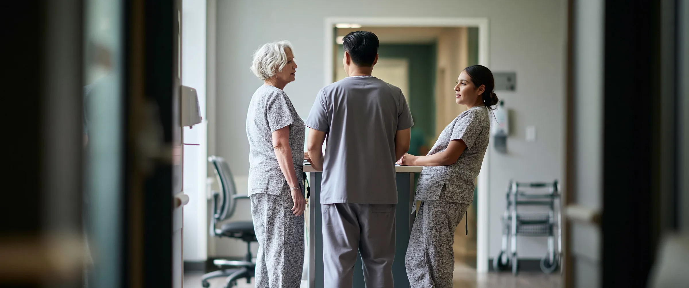 Three care staff at a handover station, shot from down the corridor