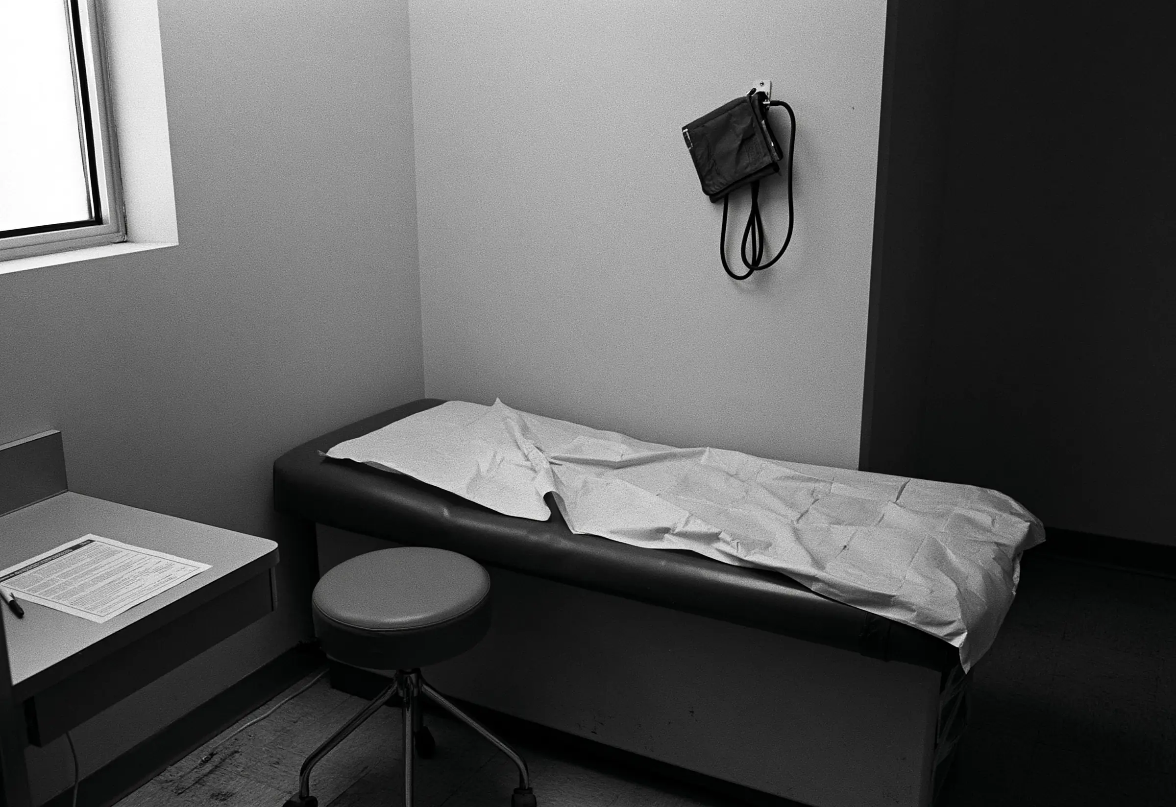 An empty examination room, the paper cover on the table creased where someone sat, a stool rolled aside and a printed sheet on the counter
