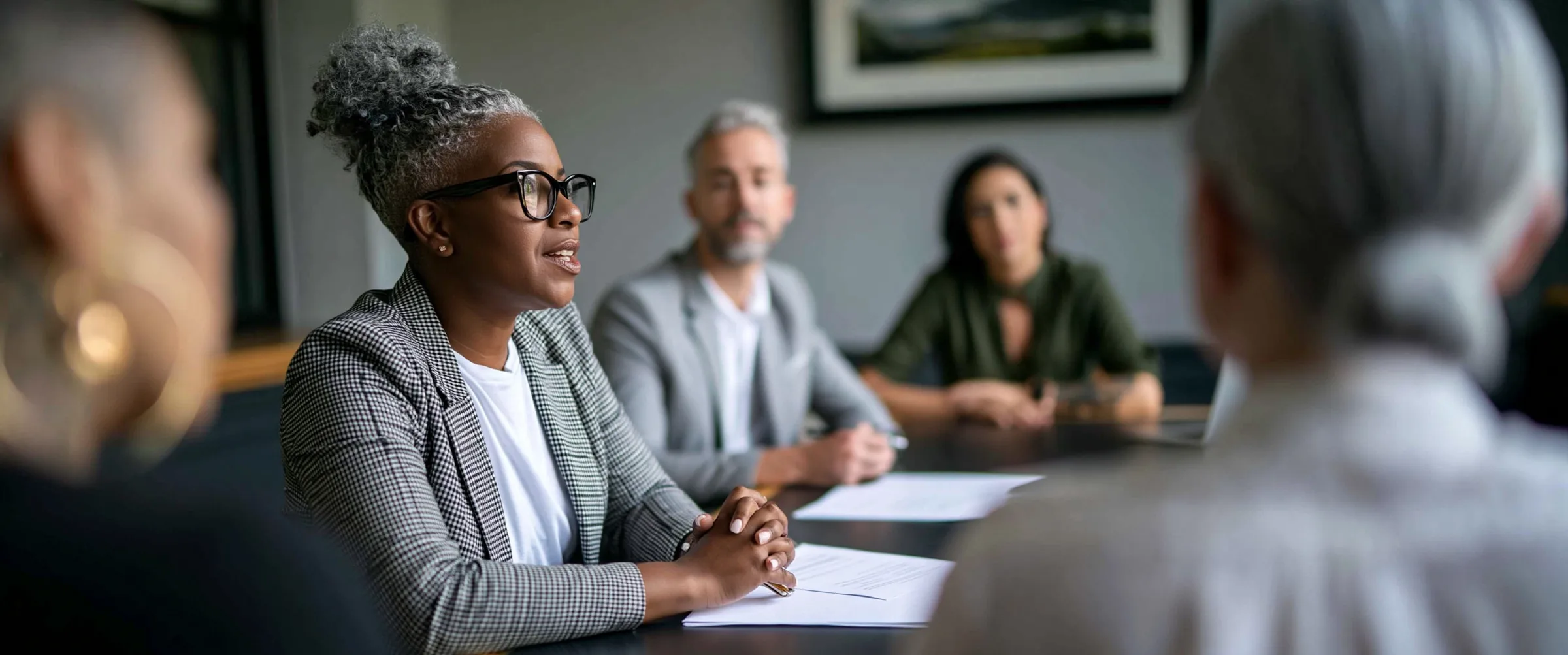 Five colleagues around a meeting table seen past two people in the foreground, one of them speaking