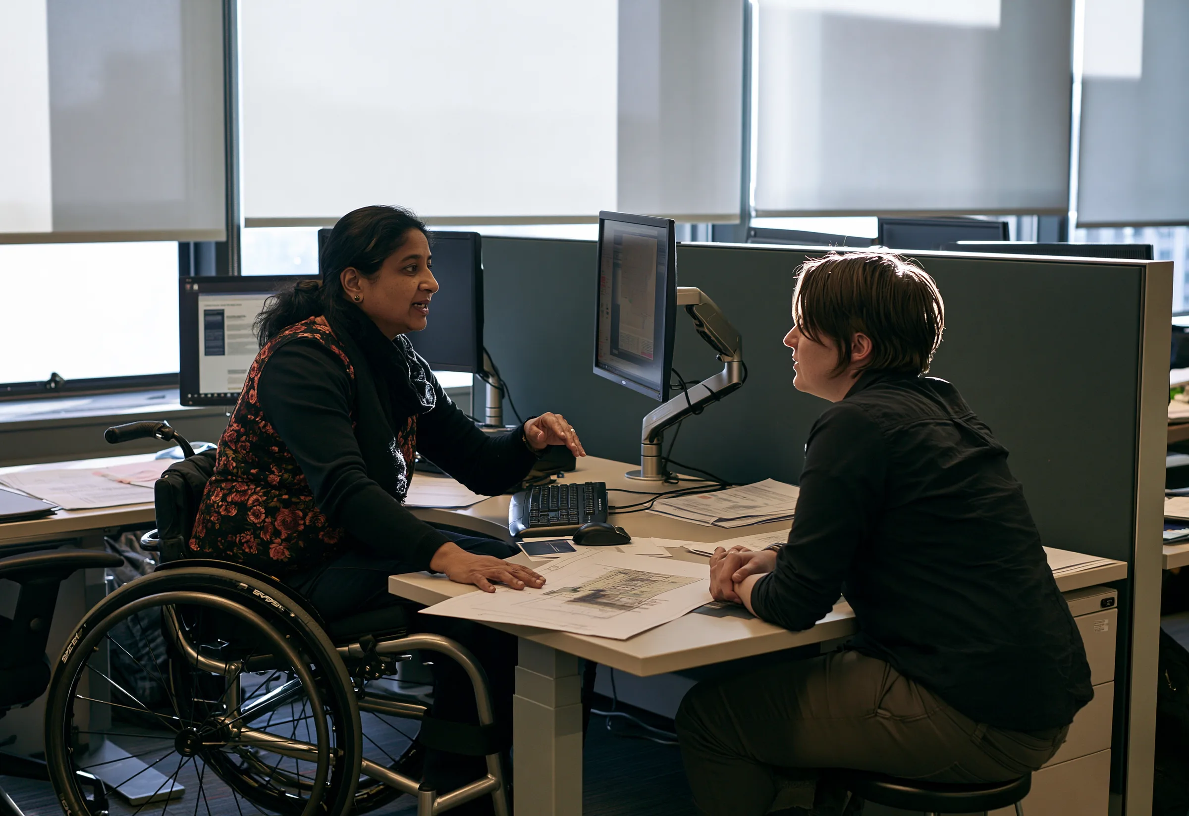 Two colleagues at a desk, one a wheelchair user, working over a drawing together